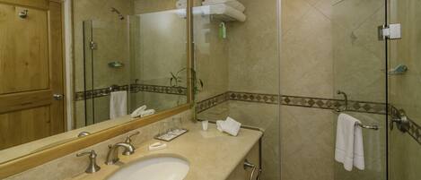 Une salle de bain équipée d’un lavabo, d’un miroir, d’une douche en verre et d’un porte-serviettes.