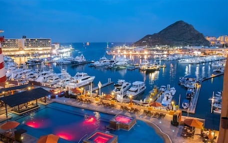 A marina with boats docked, a pool area with umbrellas, and a mountain in the background.