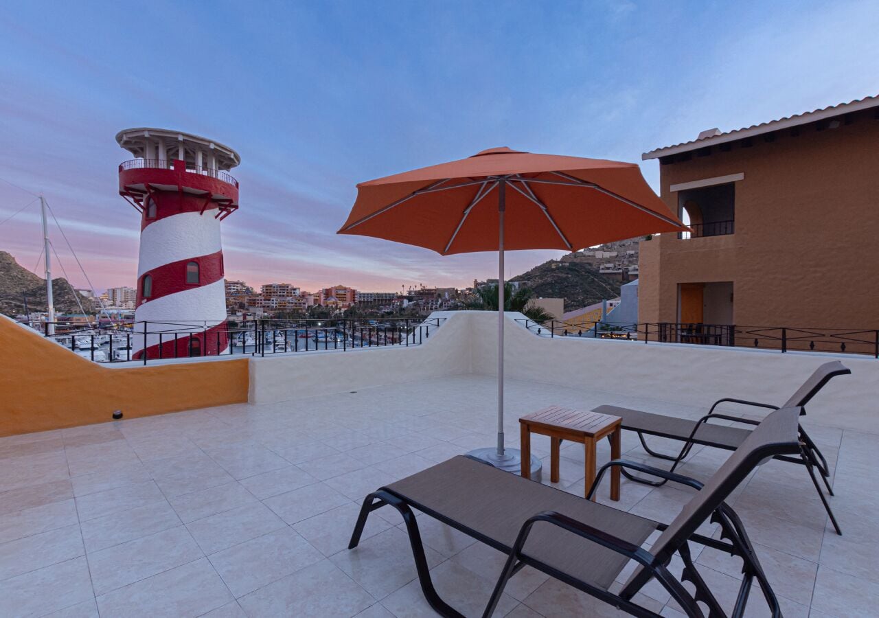 A rooftop terrace with a red and white lighthouse, a large orange umbrella, and several lounge chairs.