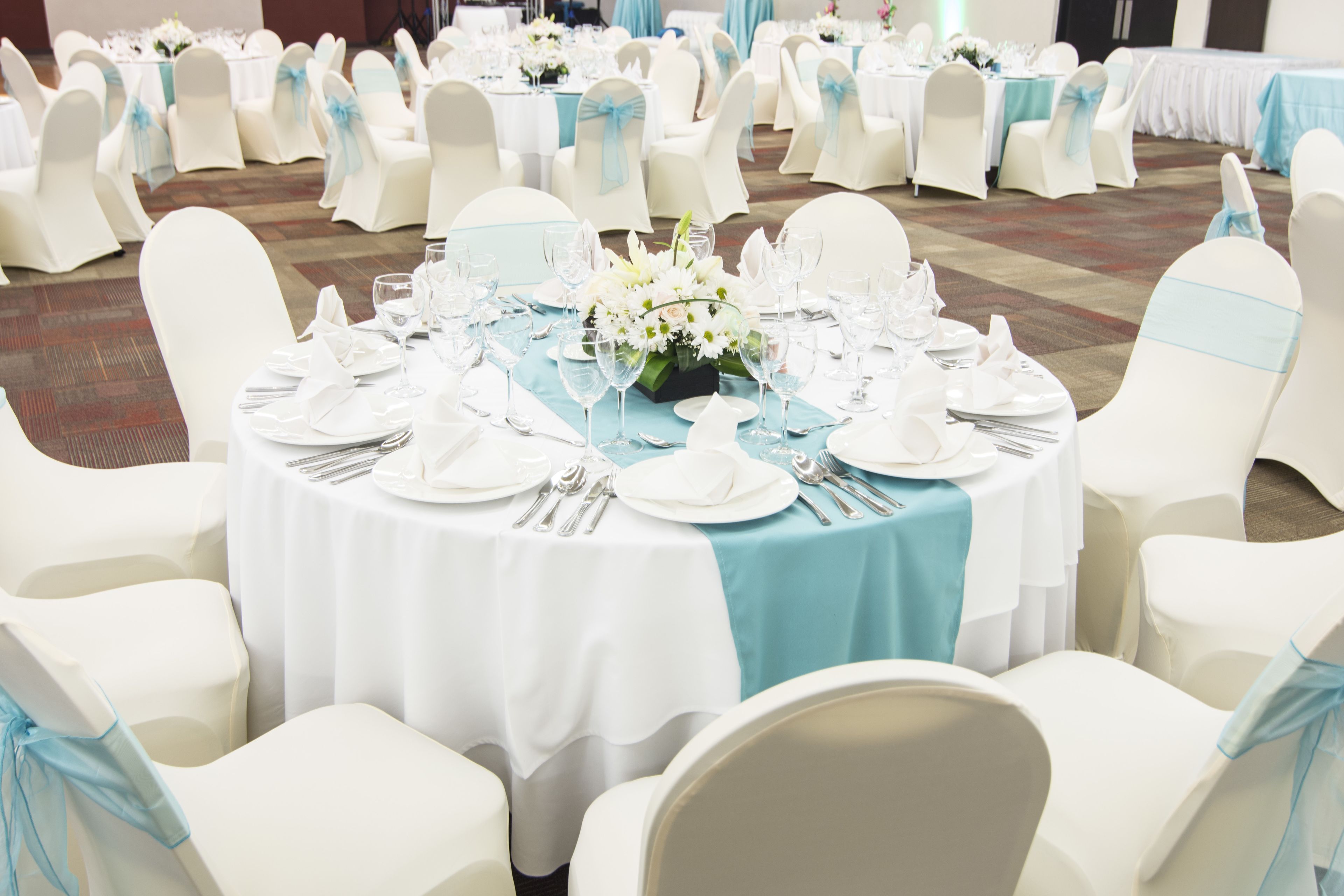 A banquet hall with round tables set for a formal event, surrounded by white chairs with blue sashes.