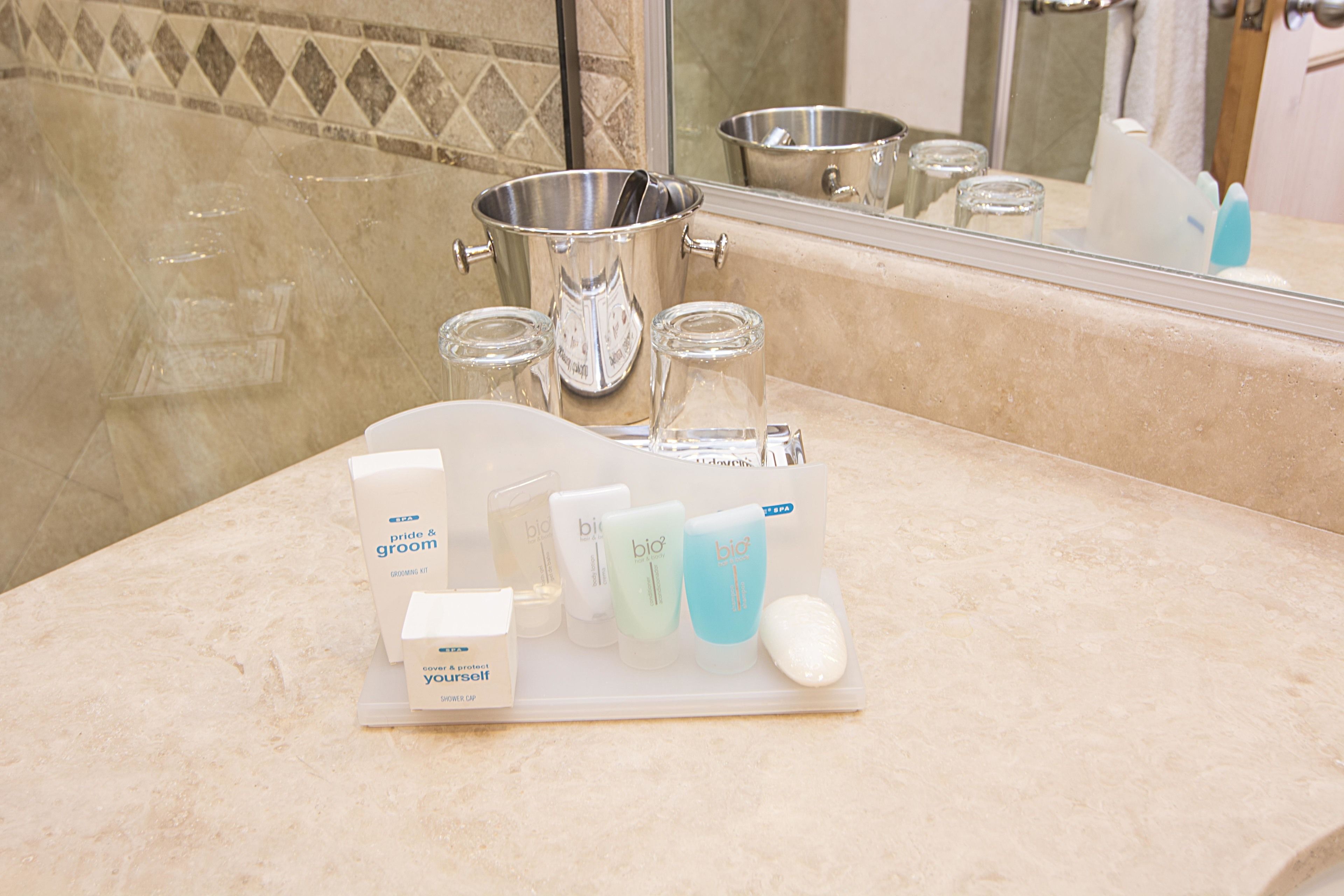 Un tocador de baño con espejo, lavamanos y encimera con un kit de aseo.