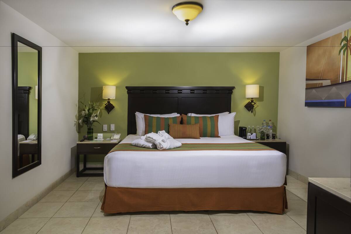 Habitación de hotel con una cama grande, dos mesitas de noche, un tocador, un espejo y una lámpara en el techo.