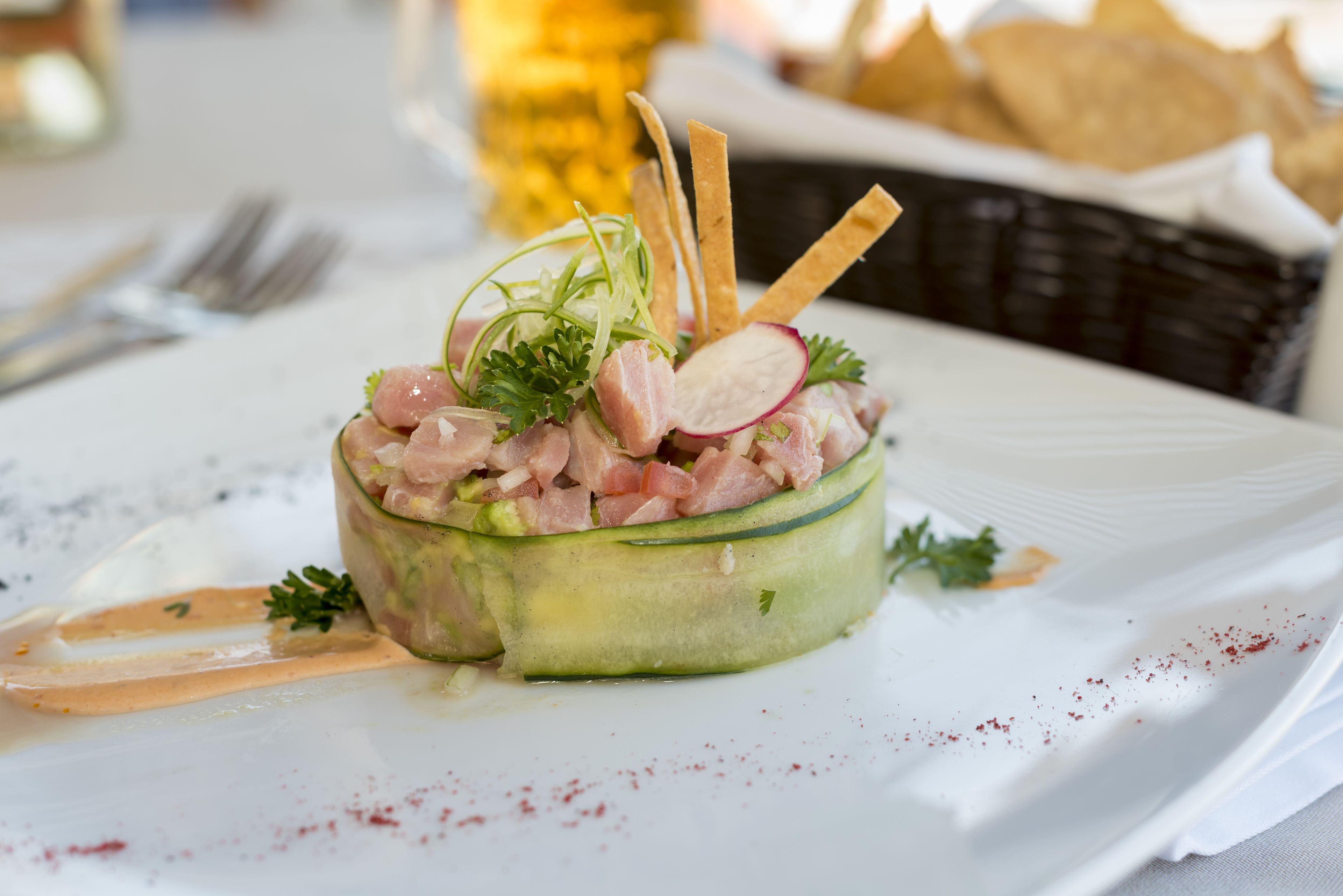 A dish of raw fish salad with crackers and herbs on a white plate.
