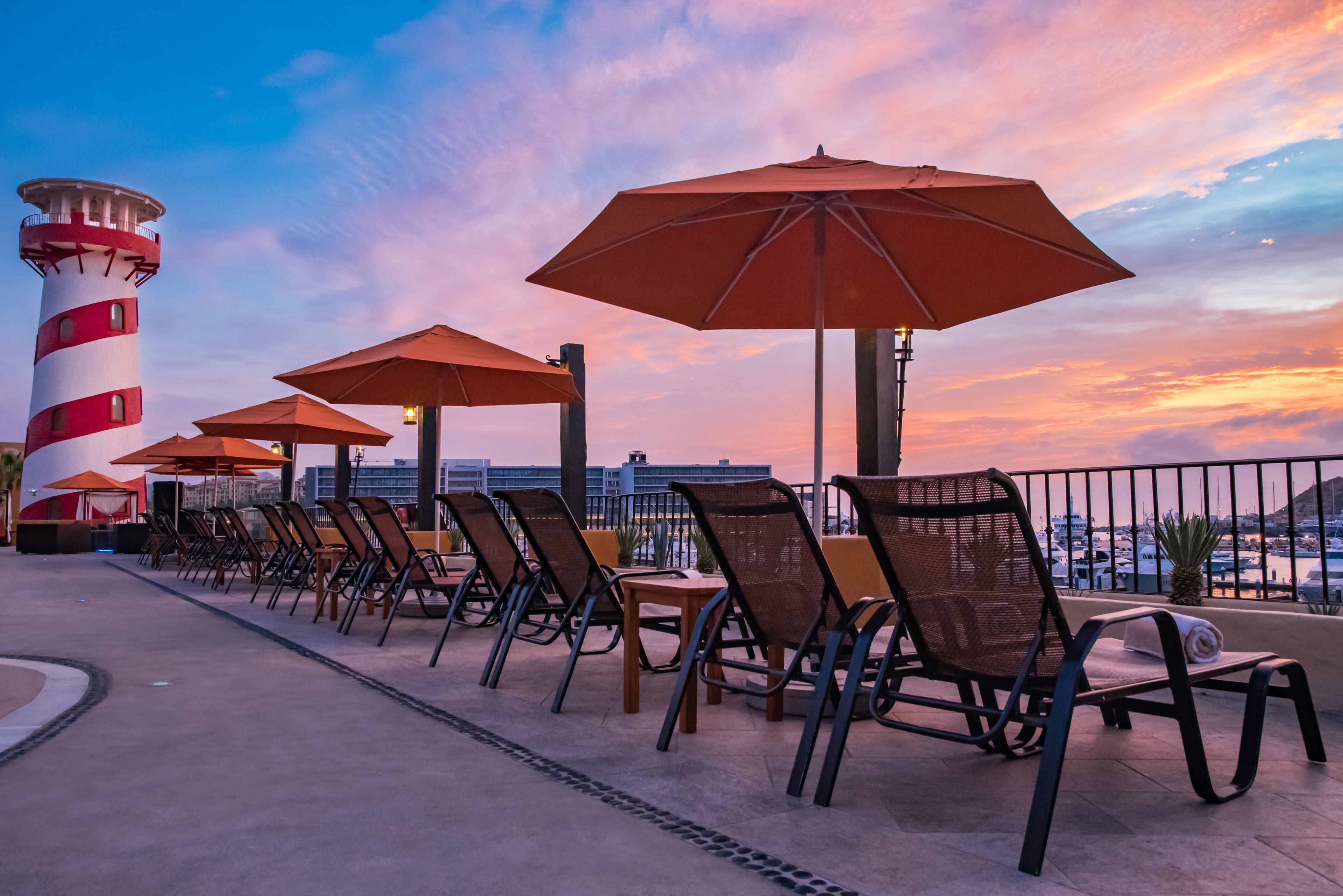 Une rangée de chaises et de parasols sur une terrasse offrant une vue sur les gratte-ciel d’une ville et un phare.