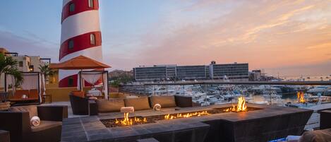 Una terraza en la azotea con asientos al aire libre, una chimenea y vistas a barcos y un edificio al fondo.