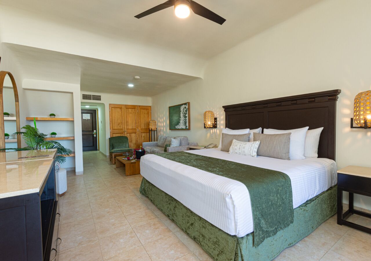 A spacious bedroom with a large bed, a desk, and a kitchenette area.