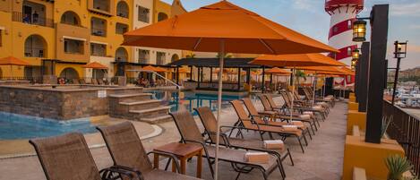 A poolside area with lounge chairs and umbrellas, a pool, and a building with arched balconies.