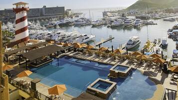 Un puerto deportivo con varios yates amarrados, una piscina con tumbonas y un faro.