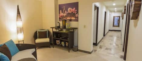 A hallway with a wicker sofa, a small table with a lamp, and a shelf with decorative items.
