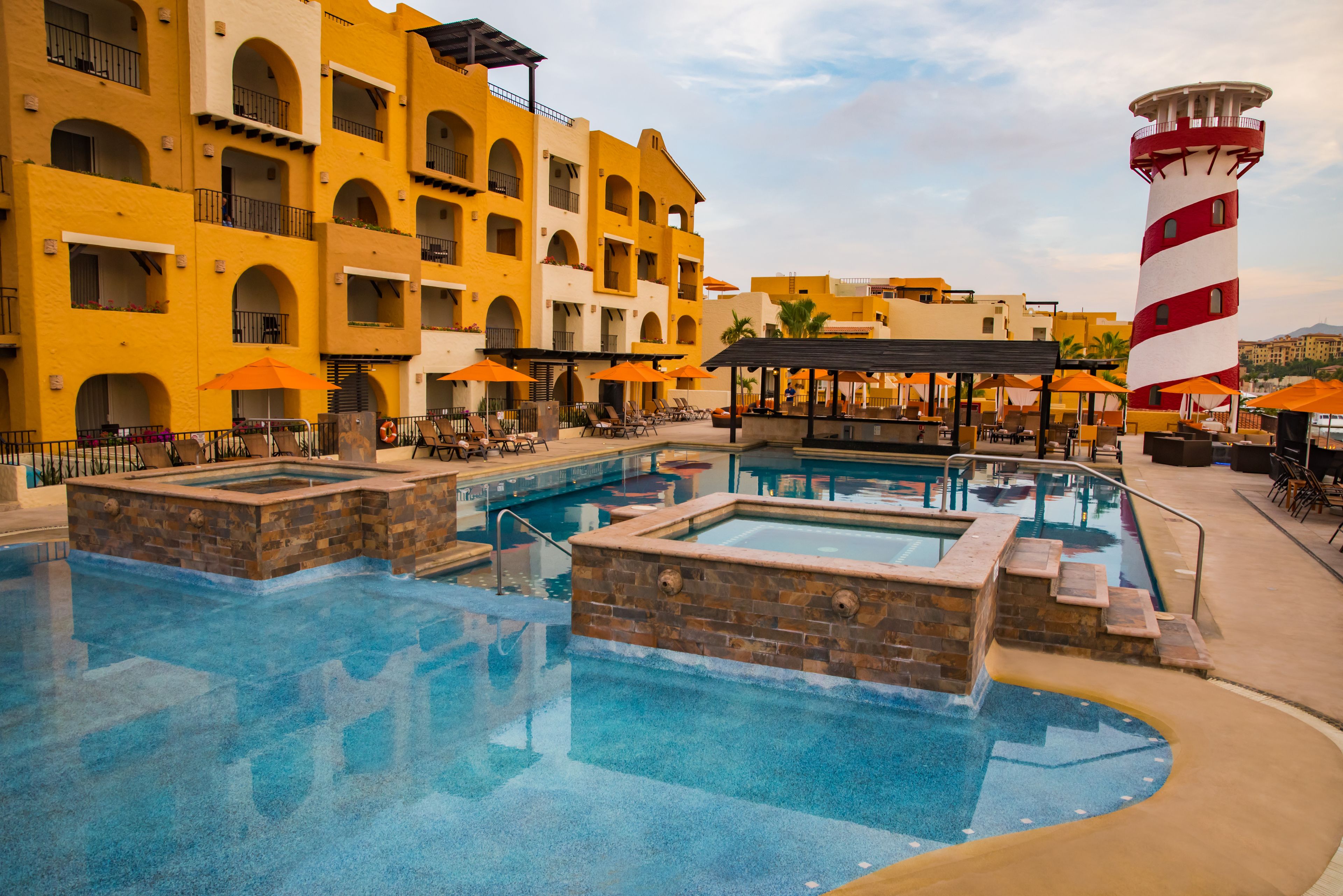 Um hotel com área de piscina, várias varandas e um farol ao fundo.