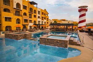 Um hotel com área de piscina, várias varandas e um farol ao fundo.