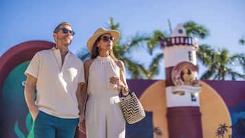 Una pareja de pie frente a un mural con un faro y palmeras.