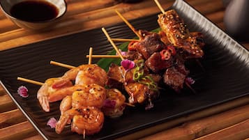 A plate of skewered shrimp and meat, garnished with sesame seeds and chili, served on a black rectangular plate.