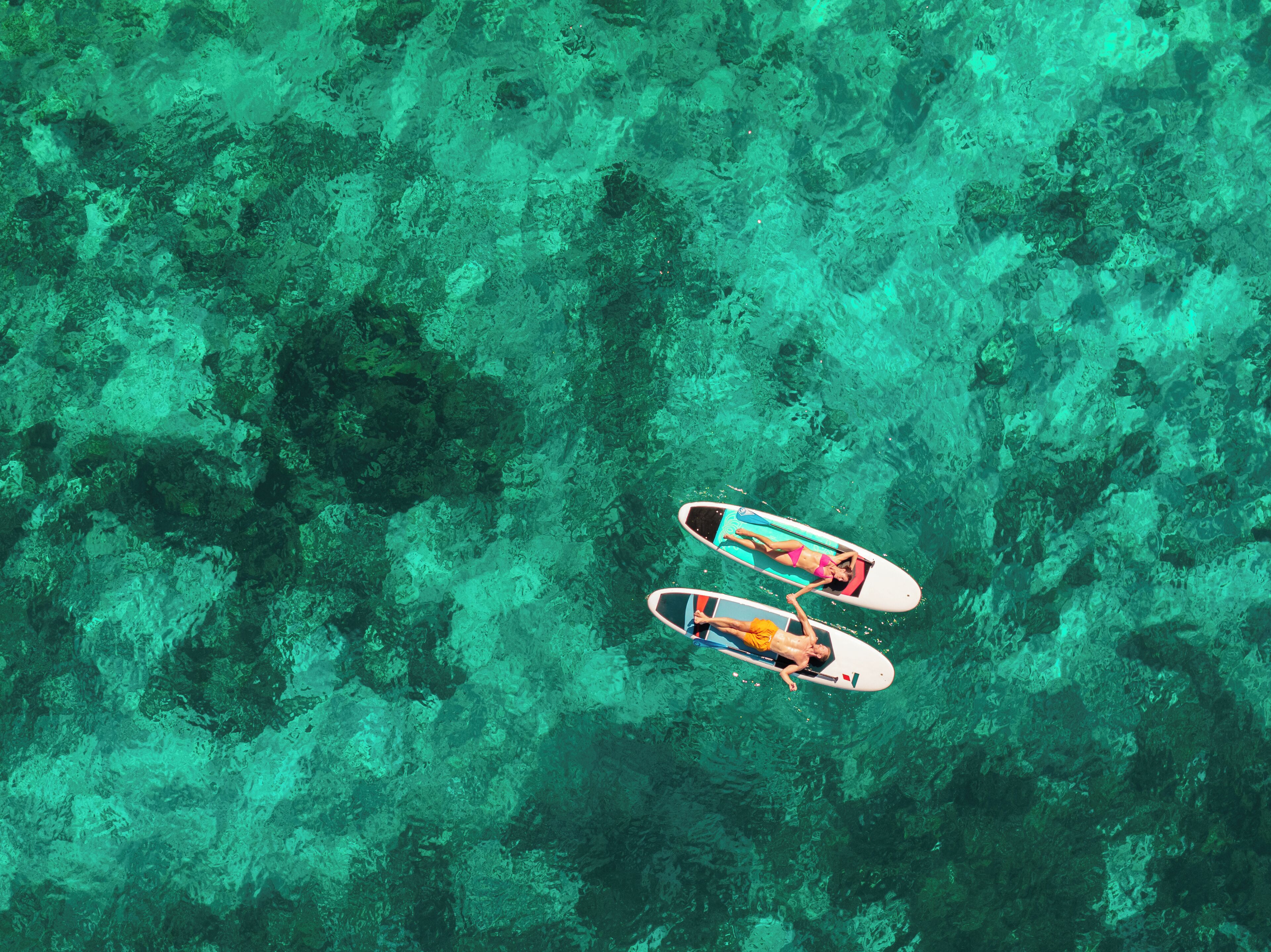 An aerial view of a clear turquoise sea with two paddleboards.