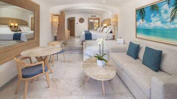 A hotel room with a bed, a sofa, a dining table with chairs, a coffee table, and a large painting of a beach.
