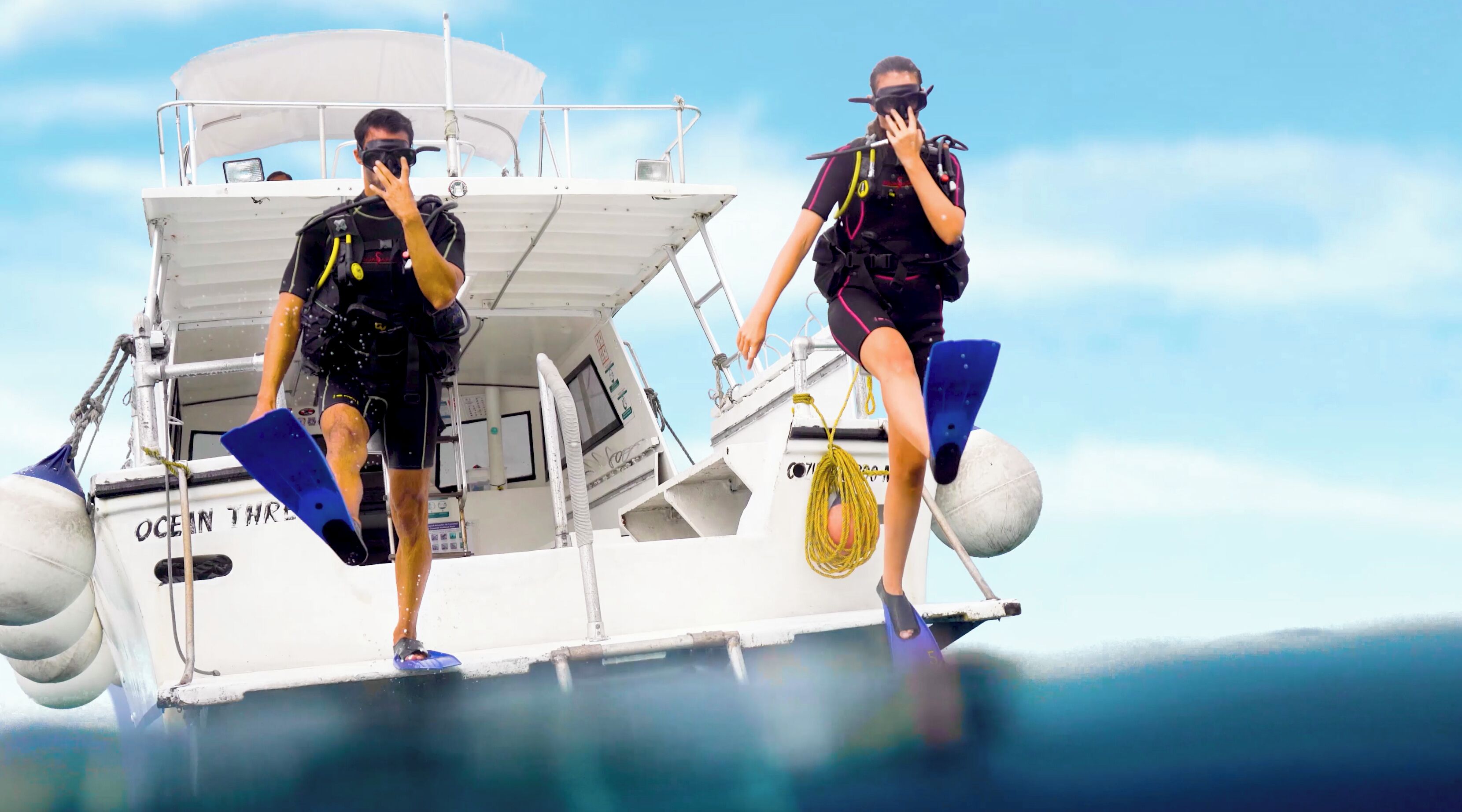 Two individuals on a boat with a cabin, equipped with diving gear and flippers.