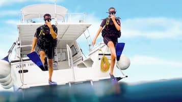 Two individuals on a boat with a cabin, equipped with diving gear and flippers.