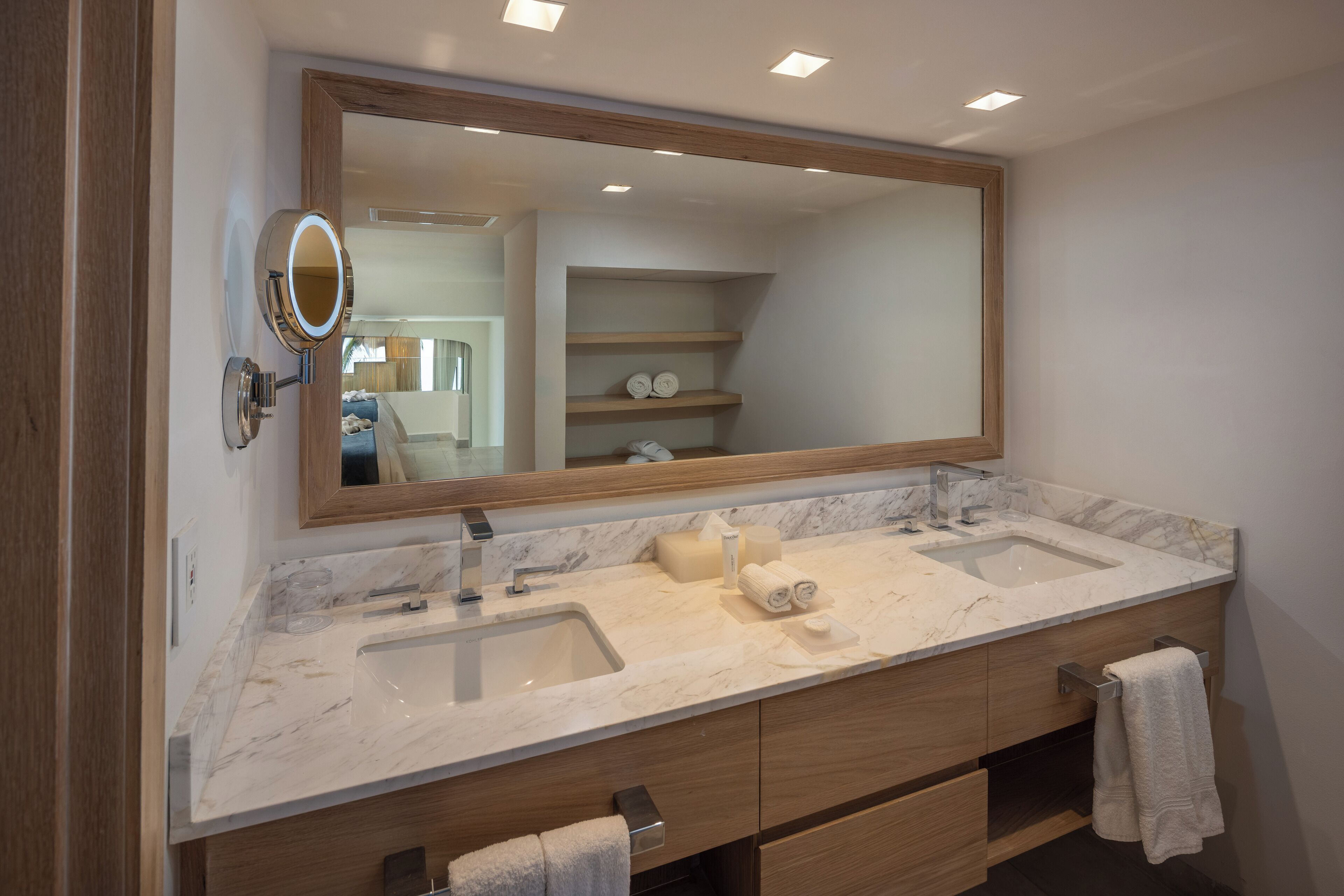 Un baño moderno con dos lavamanos, un espejo grande, armarios de madera y un perchero para toallas.