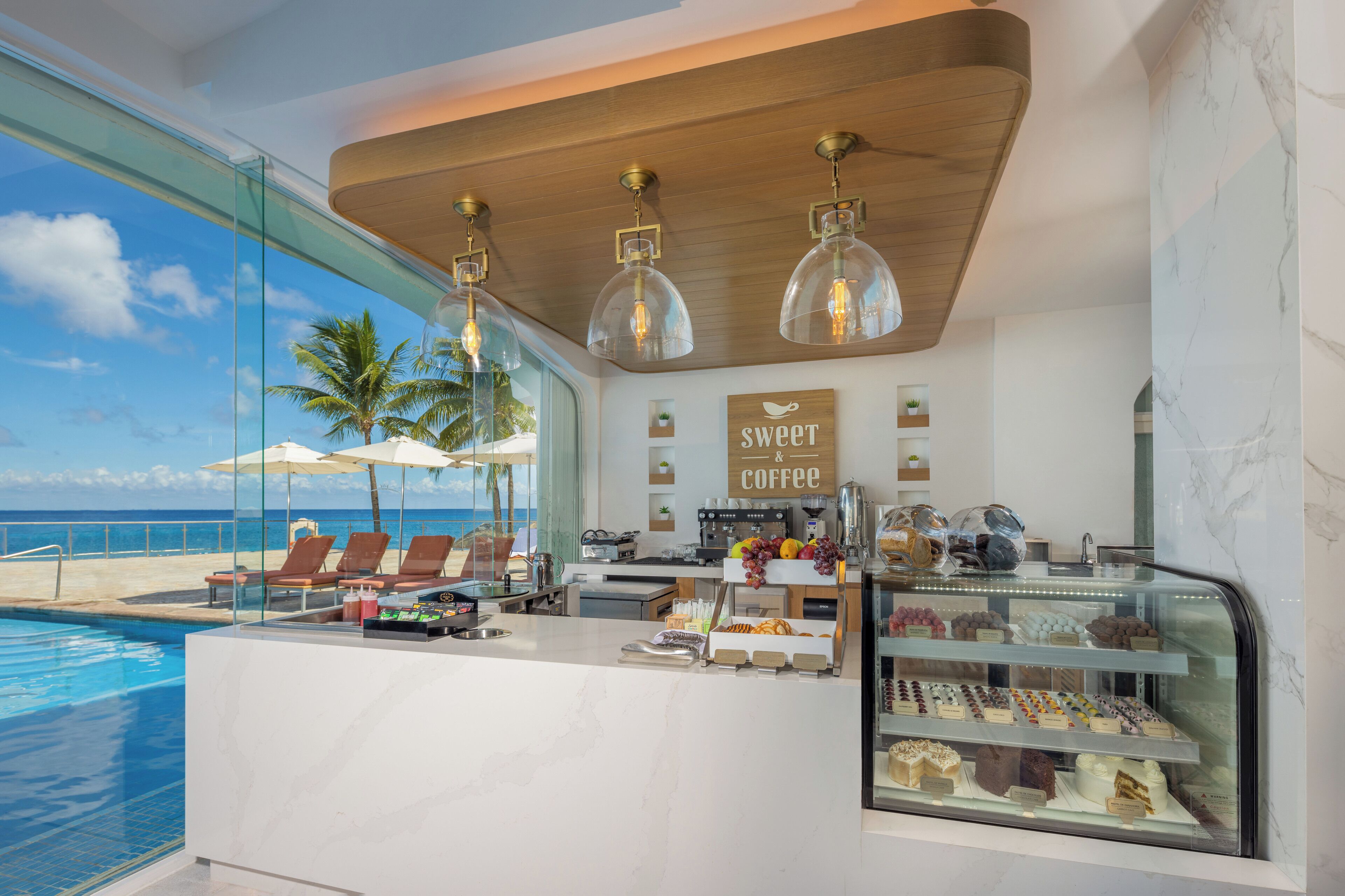 A modern bar with a view of the ocean, a sign reading "sweet coffee", and a glass display case with pastries.