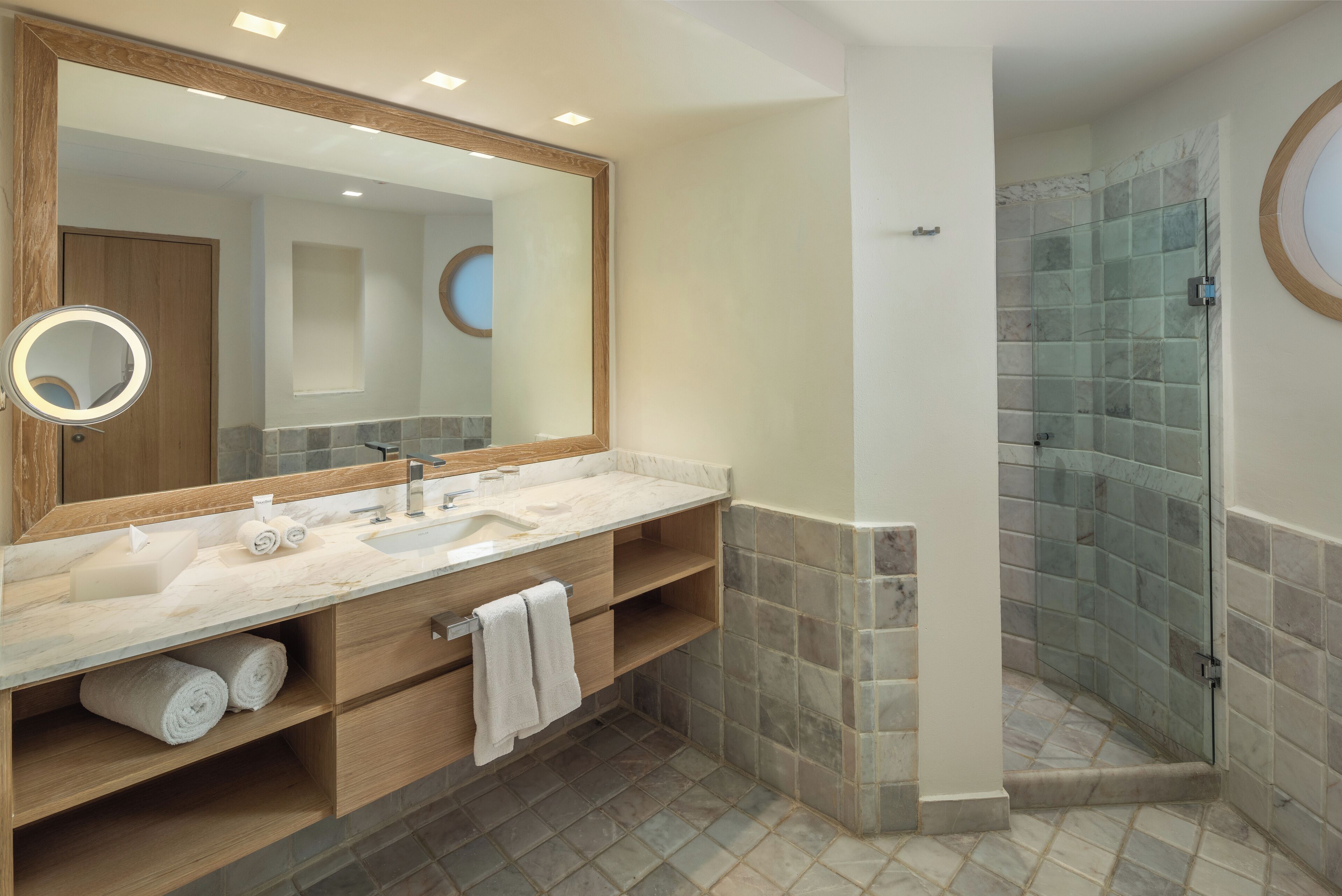 A modern bathroom with a large mirror, two sinks, a shower enclosure, and a wooden vanity.