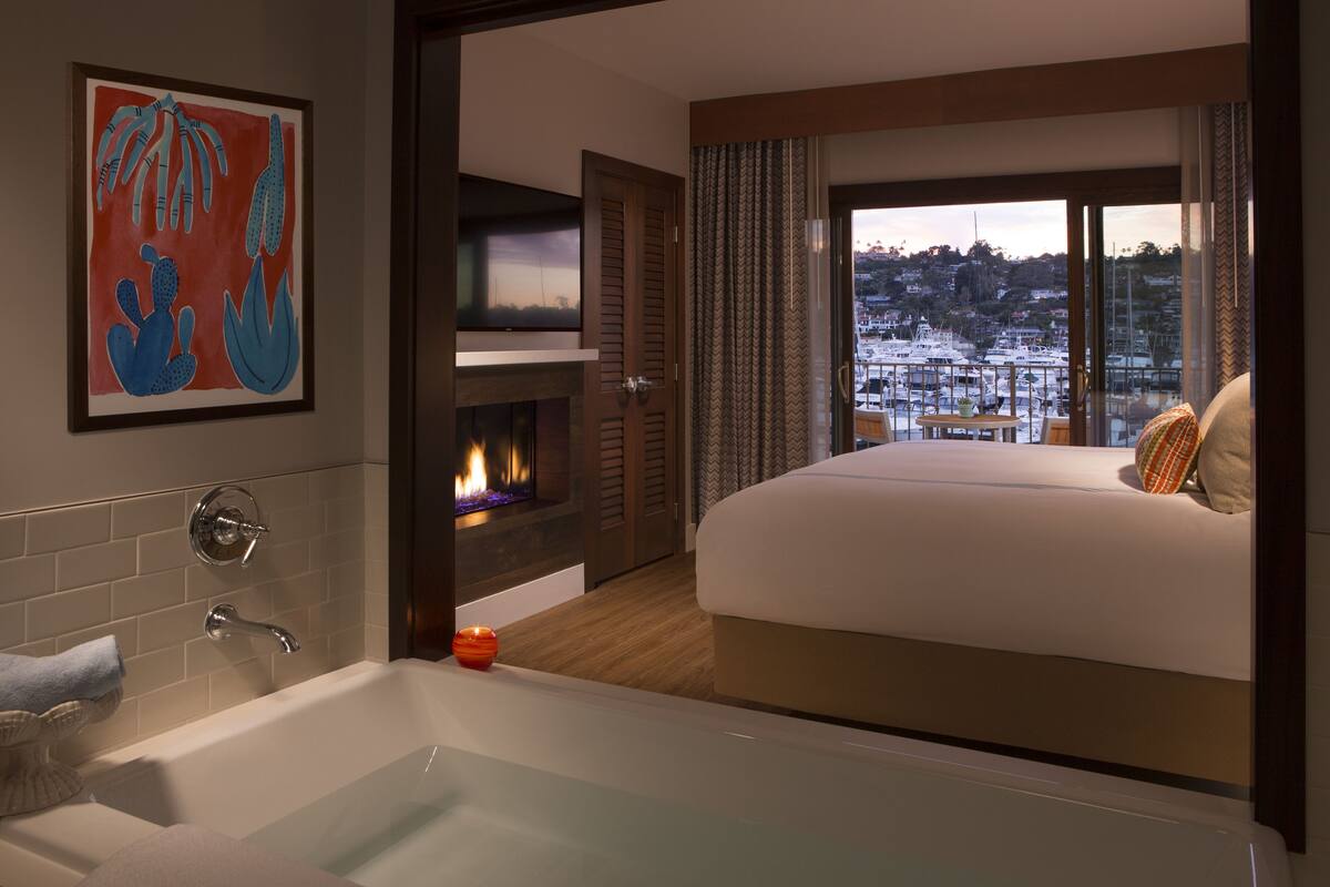 Une chambre d’hôtel avec un grand lit, une baignoire, une cheminée et un balcon offrant une vue sur les bateaux.