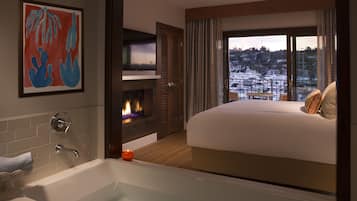 A hotel room with a large bed, a bathtub, a fireplace, and a balcony with a view of boats.