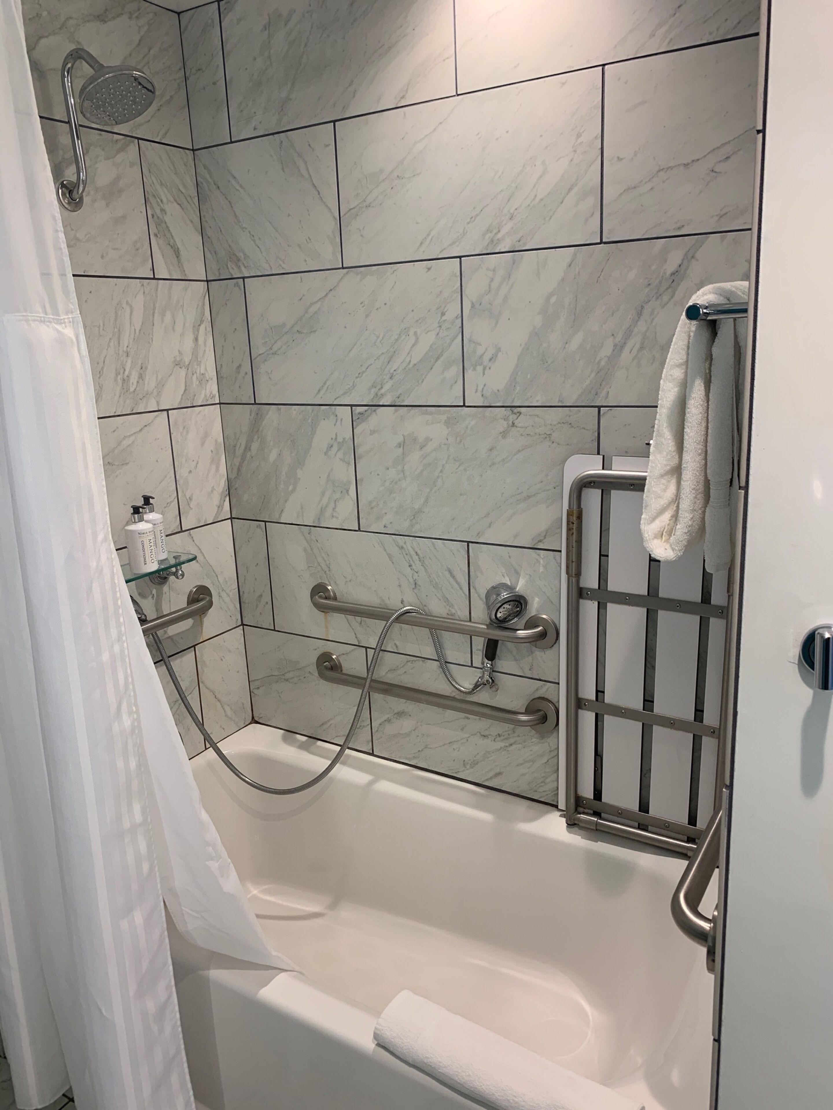 A bathroom with a bathtub, a showerhead, a towel rack, and a handrail.
