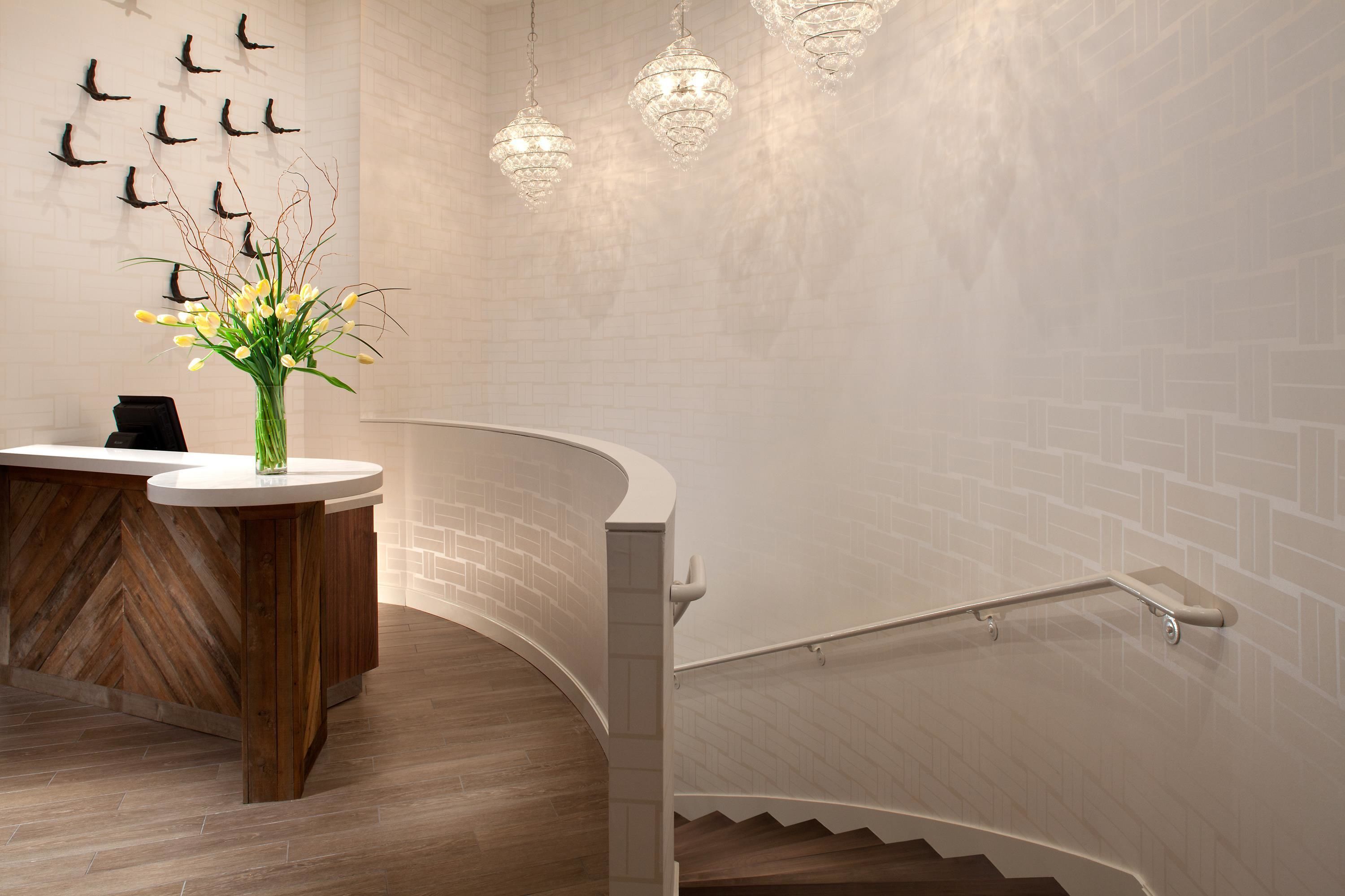 A modern reception area with a curved desk, a vase of flowers, and a staircase with a railing.