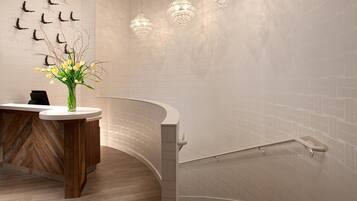 A modern reception area with a curved desk, a vase of flowers, and a staircase with a railing.