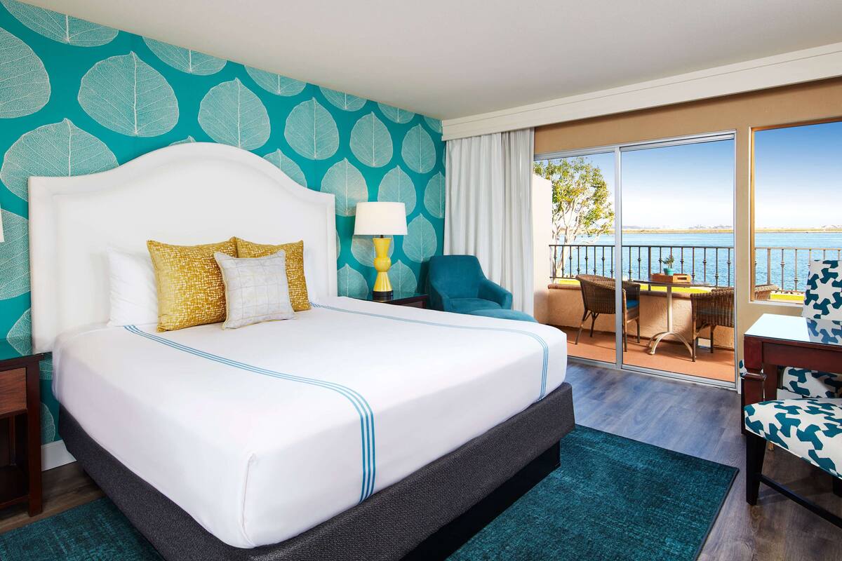 Une chambre d’hôtel dotée d’un grand lit, d’un balcon avec vue sur la mer et d’un coin repas aménagé avec du mobilier d’extérieur.