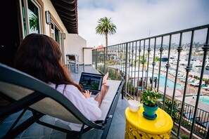 Iemand gebruikt een laptop op een balkon met uitzicht op een jachthaven met boten en een zwembad.
