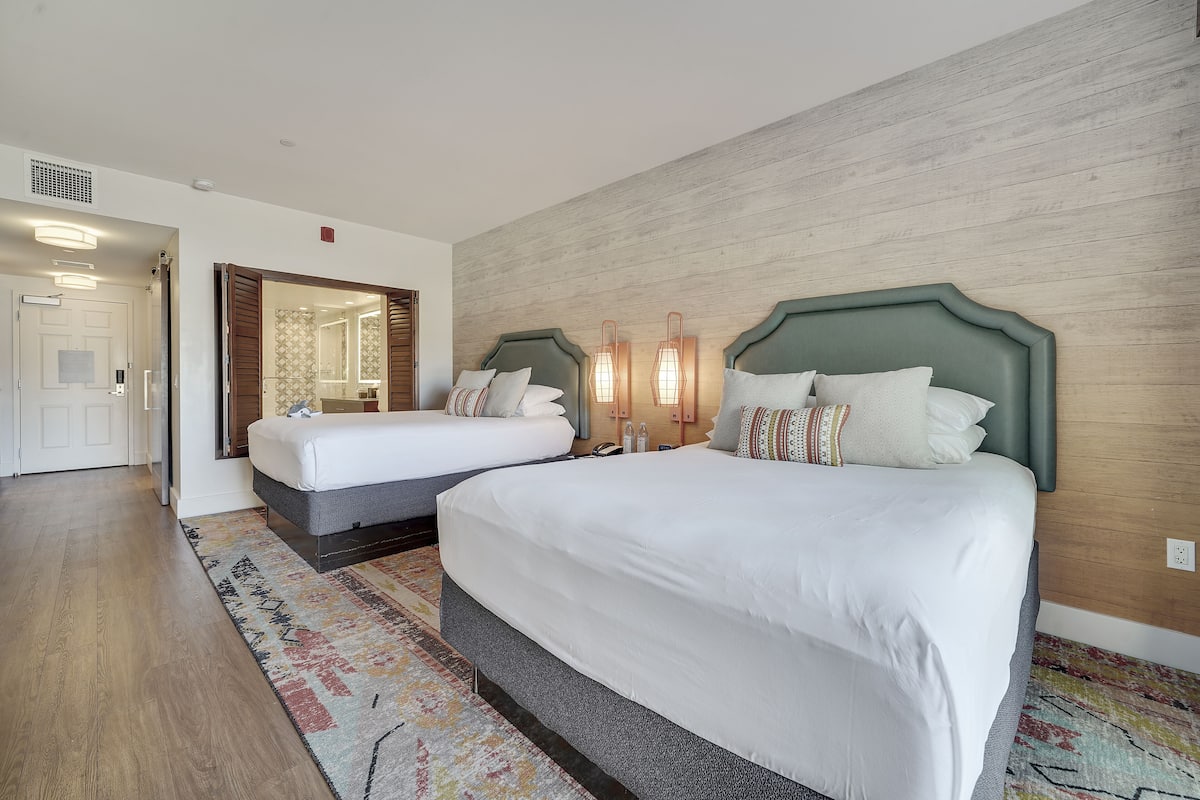 Une chambre d’hôtel avec deux lits, un grand miroir et un mur décoratif en bois.