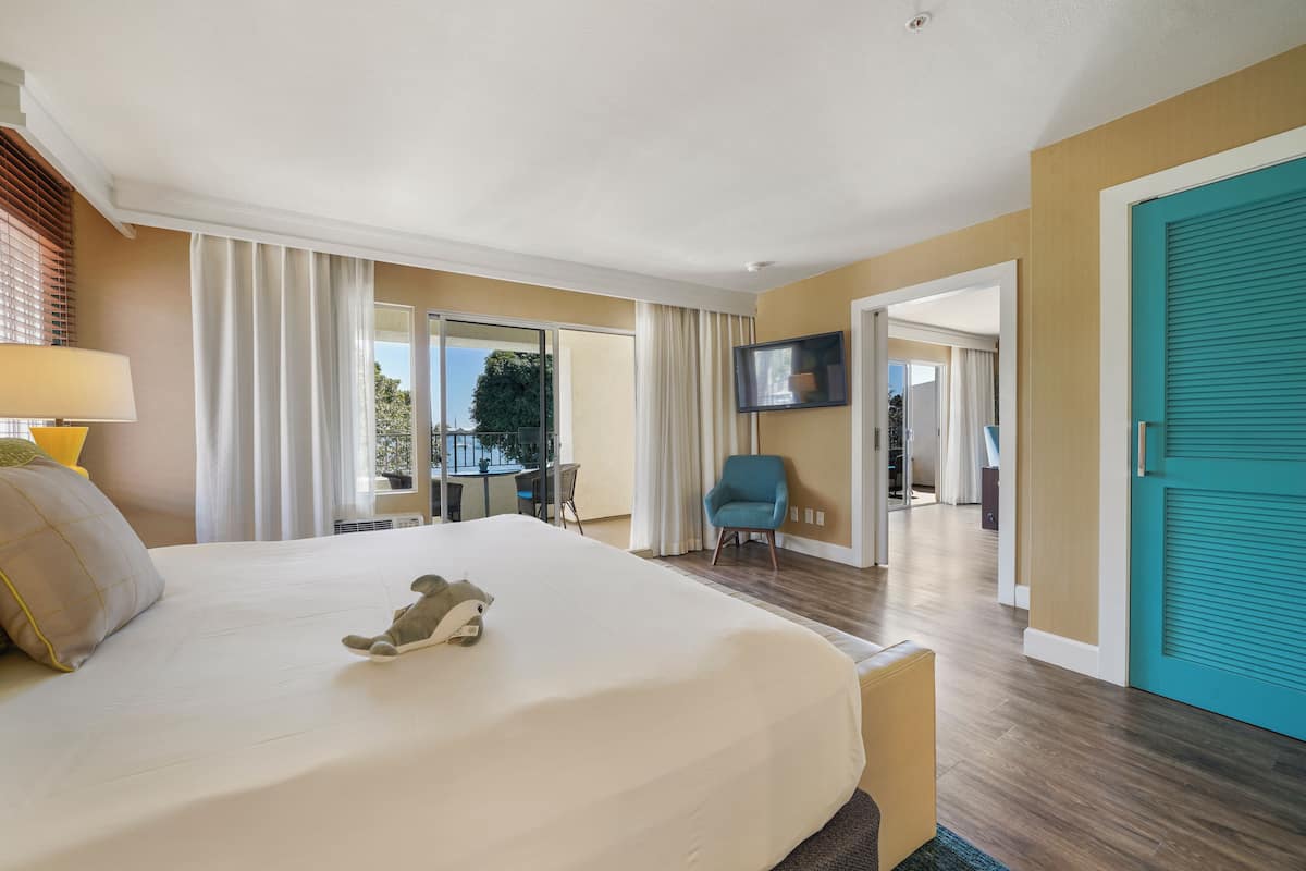 Une chambre d’hôtel avec un grand lit, un bureau, une chaise, une télévision et un balcon avec des rideaux.