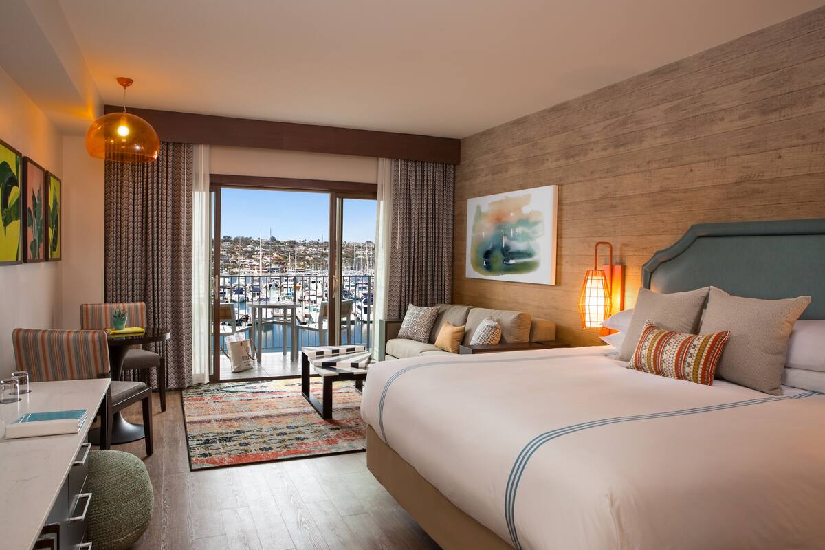 Une chambre d’hôtel avec un grand lit, un bureau et une vue sur le paysage urbain par la fenêtre.