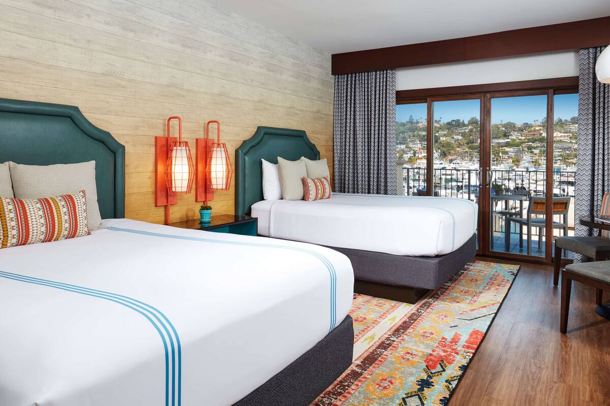 Une chambre d’hôtel avec deux lits, une grande fenêtre donnant sur le port de plaisance et un balcon avec une table et des chaises.