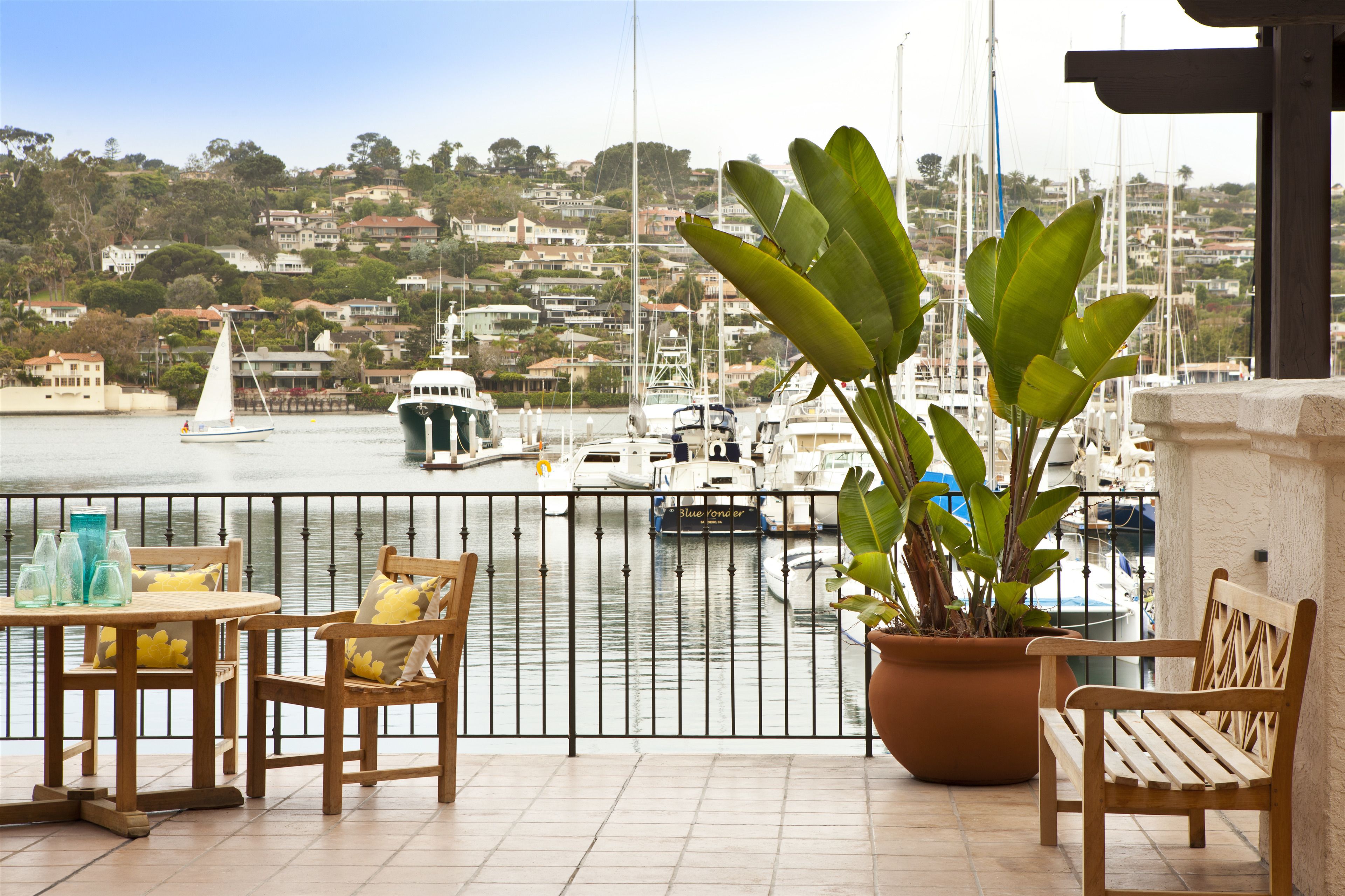 Un balcon donnant sur un port de plaisance, une table avec des chaises et une plante en pot.