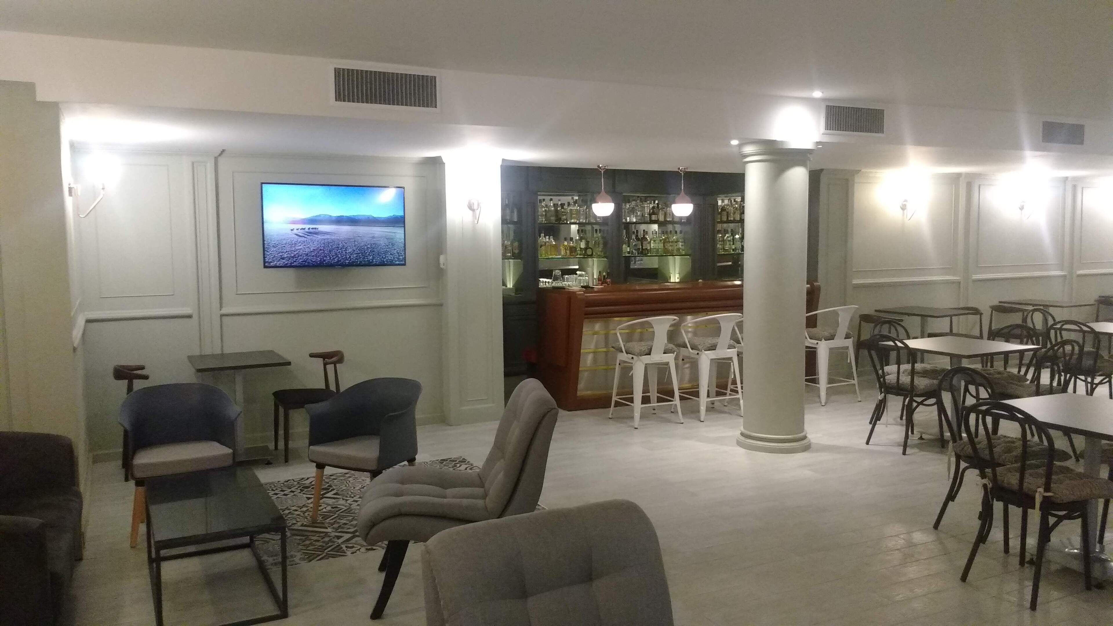 A spacious lounge area with a bar, multiple seating options including chairs and tables, and a large flat-screen TV mounted on the wall.