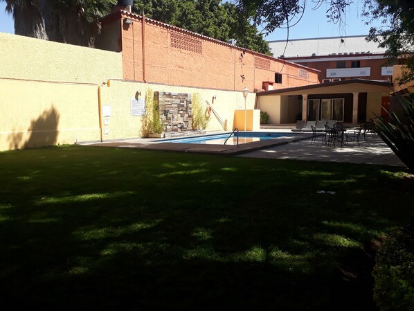 A backyard with a swimming pool, a patio with chairs, and a brick wall.