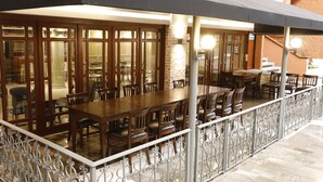 An outdoor dining area with wooden tables and chairs, a metal railing, and a brick wall in the background. - Country Plaza (Zapopan)