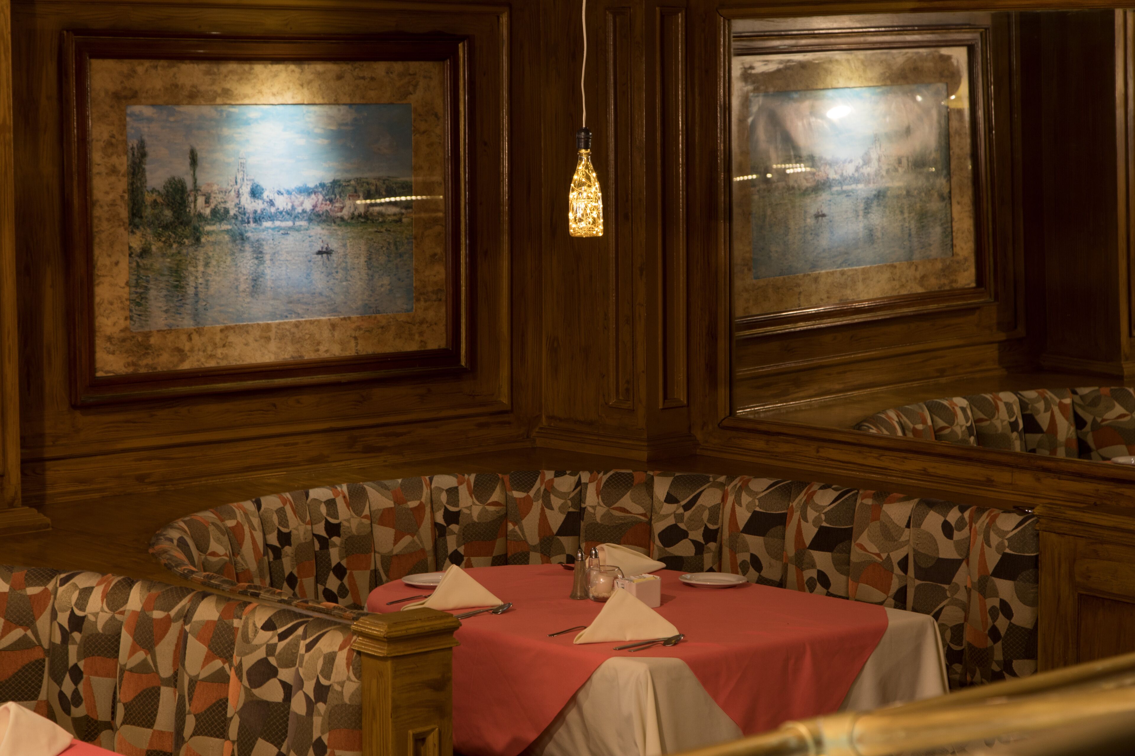 A dining area with a round table set for two, a patterned bench, and two framed paintings on the walls.