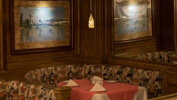 A dining area with a round table set for two, a patterned bench, and two framed paintings on the walls.