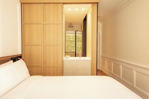 A bedroom with a large bed, a wooden wardrobe, a window with a view, and a bathroom with a shower.