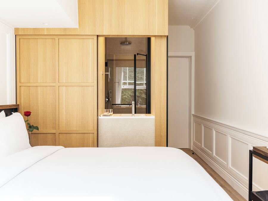 A bedroom with a large bed, wooden wardrobe, and a window with a view of the outdoors.