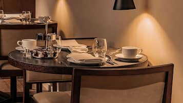 Un comedor con una mesa redonda dispuesta para dos personas, que incluye un candelabro, platos y copas. Dos lámparas de pared proporcionan iluminación.