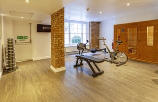 A gym with exercise equipment, a brick pillar, a wooden wall, and a television on the wall.