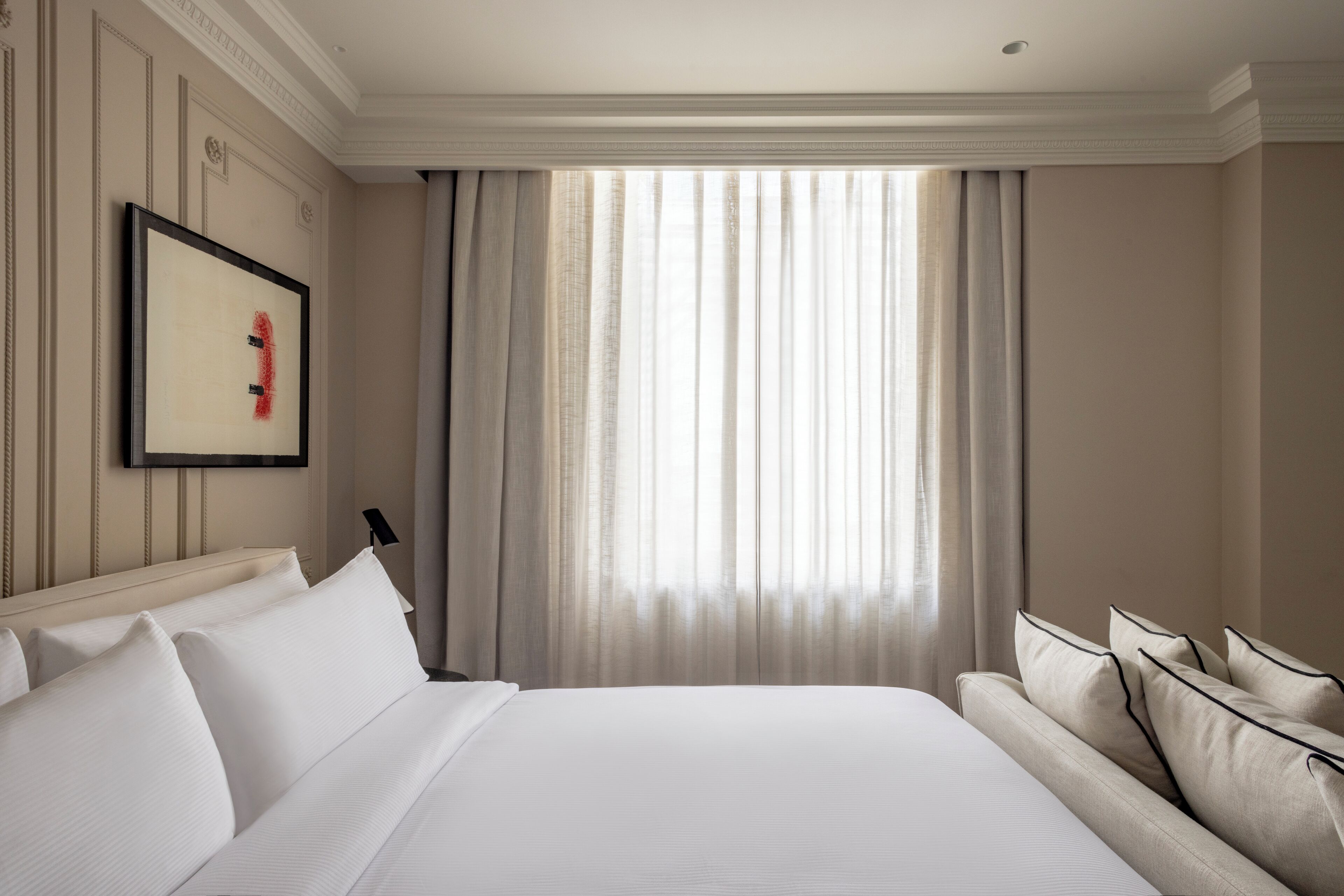 Habitación de hotel con una cama grande, un sofá, un cuadro en la pared y una ventana con cortinas.
