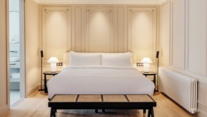 Una cama grande con ropa blanca, dos mesitas de noche con lámparas, suelo de madera y un radiador.
