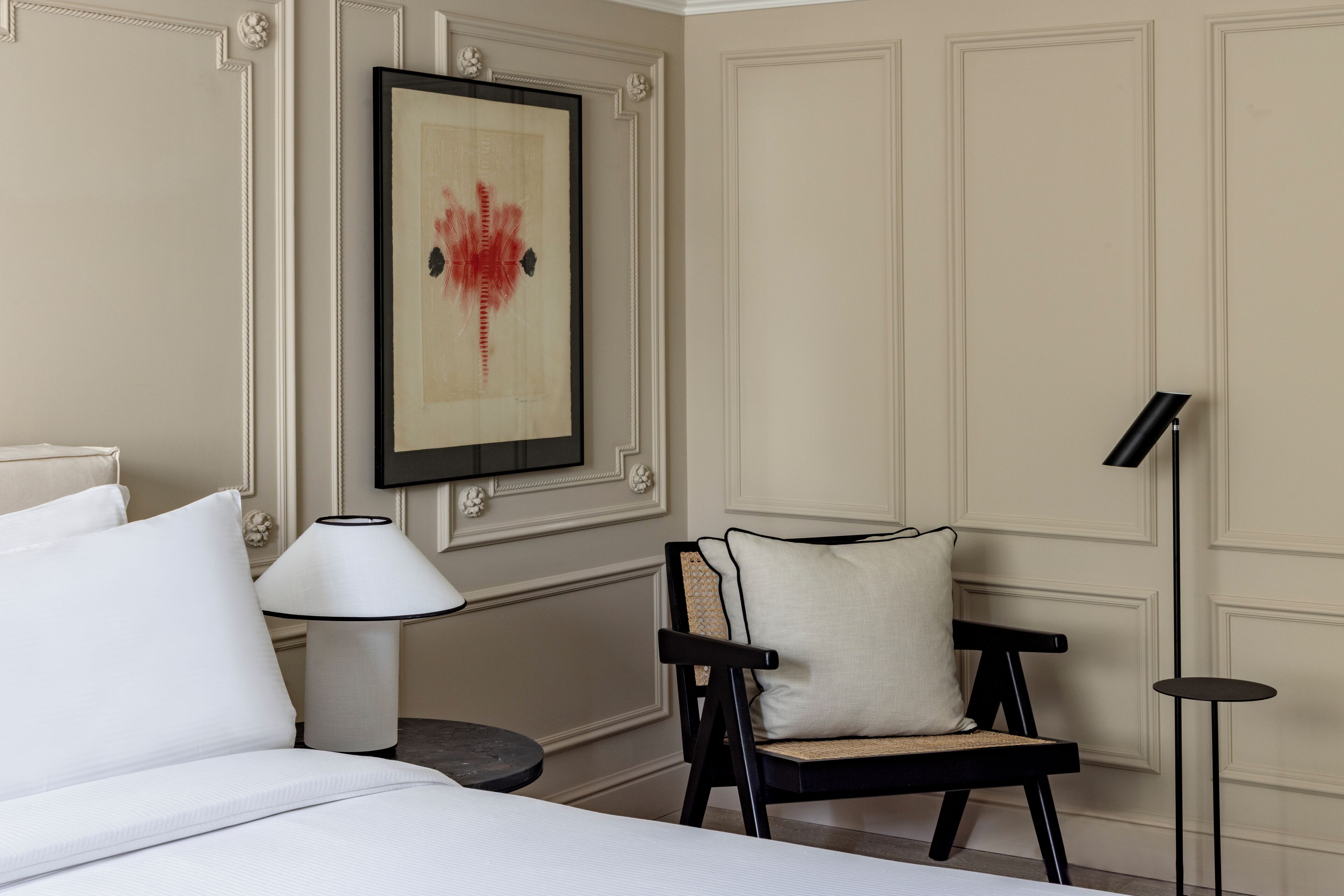 A hotel room with a bed, a chair, a lamp, and a framed artwork on the wall.