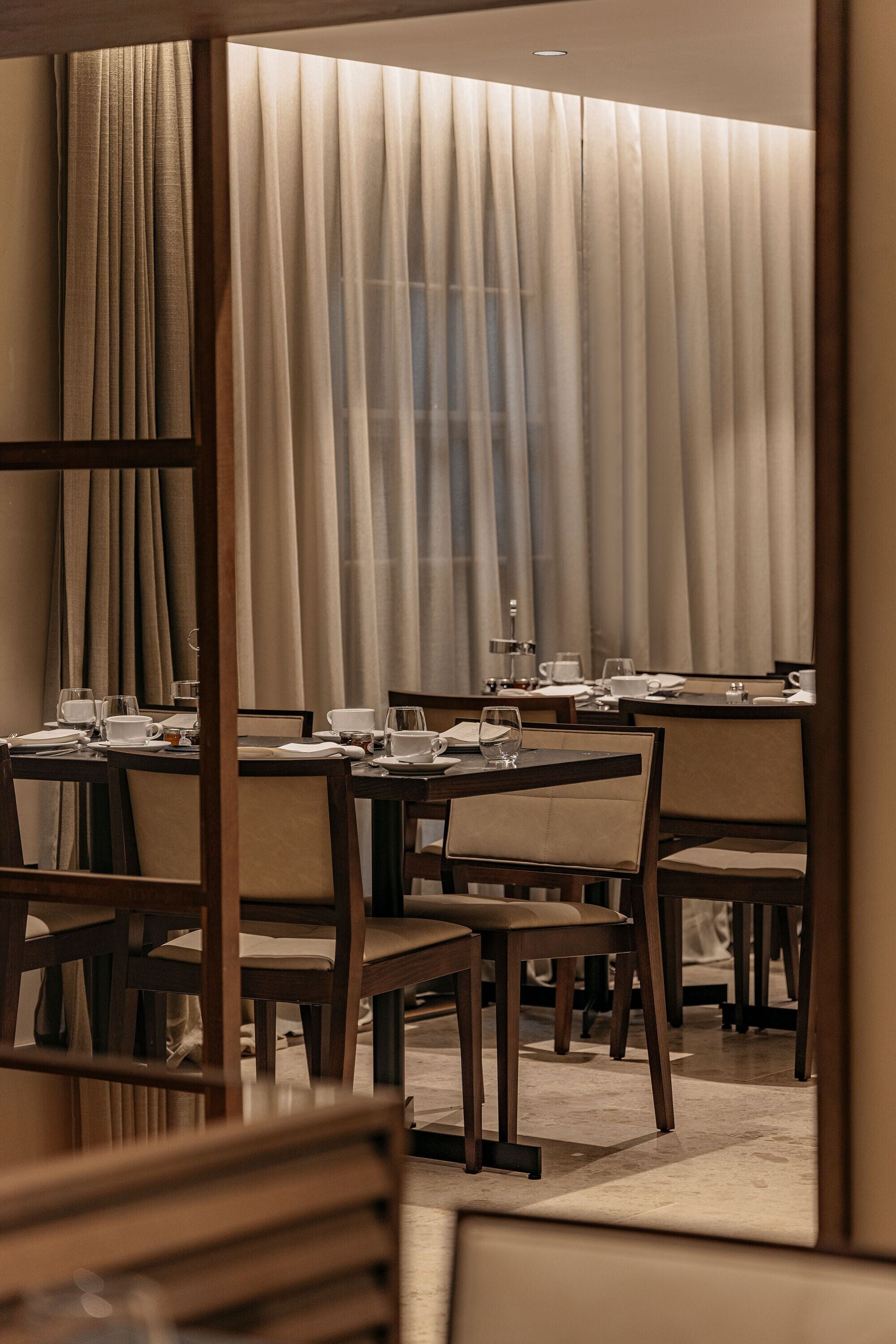 A hotel dining area with tables set for dining, chairs, and a large window with curtains.