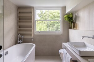 A modern bathroom with a bathtub, a sink, and a window with a view of trees.